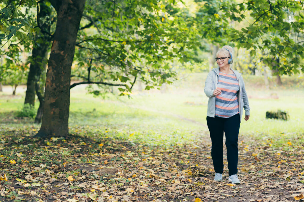 Beautiful woman, senior, running in headphones, walking in the park, playing sports