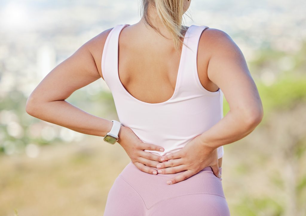 Back pain, hands and woman exercise outdoor, wellness or muscle tension. Healthy female, athlete